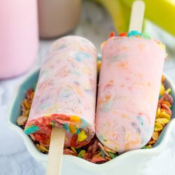 Vertical layout showing two milk and cereal popsicles filled with colorful fruity cereal flakes resting on wooden sticks