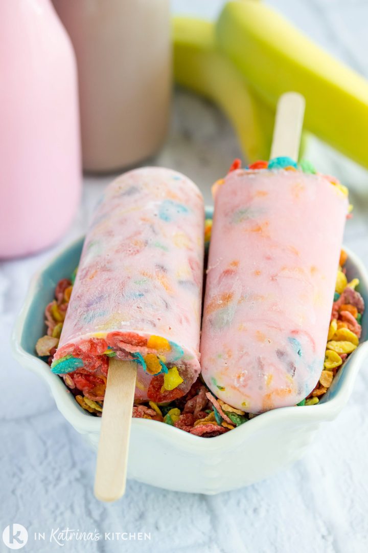 Vertical layout showing two milk and cereal popsicles filled with colorful fruity cereal flakes resting on wooden sticks