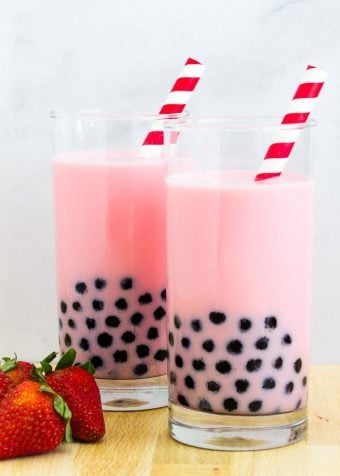 two large glasses of pink strawberry milk bubble tea with black tapioca pearls and red striped straws