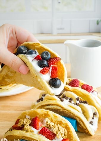 a female hand holding a pancake like a taco. The pancake is filled with fresh berries and vanilla yogurt.